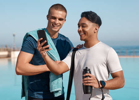 Life is better where its wetter. two young men using a smartphone before going for a swim.の写真素材