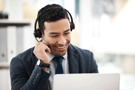 What do you need today. a young male call center agent using a laptop while working in an office.の写真素材