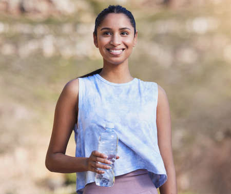 Thinking about the run. an attractive young female athlete taking a break from her outdoor run to drink some water.の写真素材