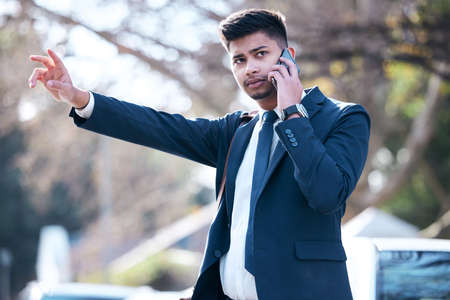 Catching a ride to success. a young businessman talking on a cellphone while hailing a cab in the...