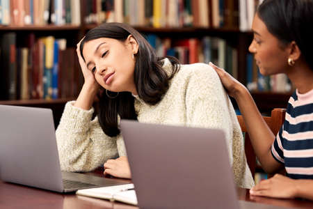 Friends are always there to comfort you when youre down. a young female student comforting her unhappy friend while studying in a library at college.の写真素材