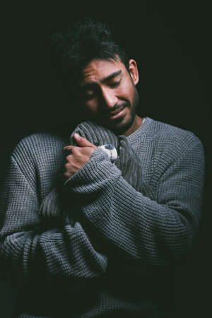 We all need a safe space to escape to. a young man looking unhappy and cuddling a stuffed animal...