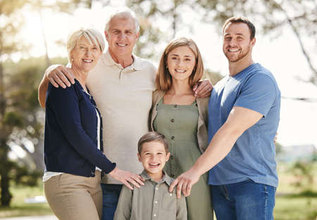Portrait of a smiling multi generation caucasian family standing close together outdoors. Adorable little boy bonding with his mother, father, grandfather and grandmother at a parkの写真素材