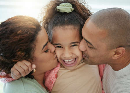 Who doesnt love being loved. an adorable little girl getting kisses on her cheeks from her parents.