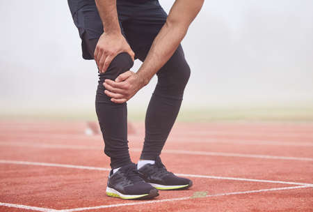 Looks like his race is run. an unrecognizable male athlete holding his knee in pain while standing...