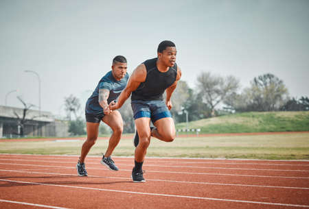 Hes done his part. Full length shot of a handsome young male athlete grabbing a baton from his teammate during a relay race.の写真素材