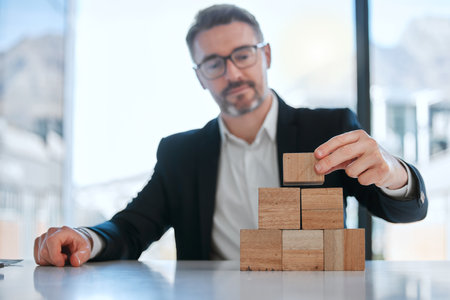 Innovation is the catalyst for change. a mature businessman working with wooden building blocks in a modern office.の写真素材