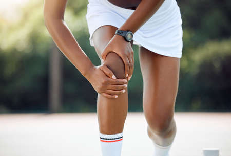 I wont be able to compete like this. Closeup shot of a sporty young woman experiencing knee pain while playing tennis outdoors.の写真素材