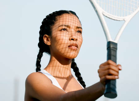 Eyes on the prize. a sporty young woman shielding her face from the sun with a tennis racket on a court.の写真素材
