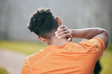 Im pretty sure this pain is coming from my upper back. an unrecognisable man standing alone and suffering from a neck injury during his outdoor workout.の写真素材