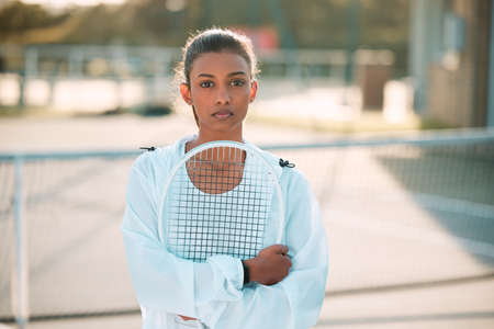I take this sport very seriously. an attractive young woman standing alone outside and posing with a tennis racket.の写真素材