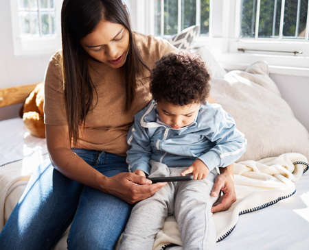 A mothers love is like no other. a young mother and son using a phone while relaxing at home.
