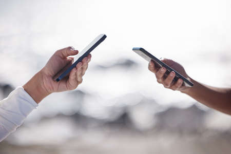 Theres always a connection to share in. Closeup shot of two unrecognisable women using cellphones outdoors.の写真素材