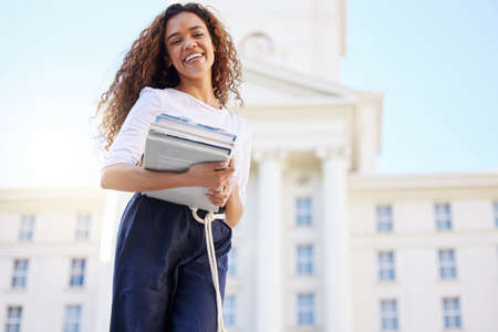 Dont worry. Be happy. a young woman carrying her schoolbooks outside at college.の写真素材