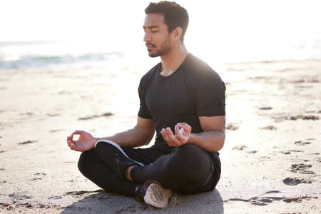 Its a matter of balance. Full length shot of a handsome young male athlete meditating on the beach.の写真素材
