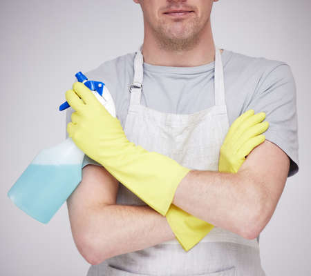 What needs cleaning today. an unrecognizable man holding a spray bottle with his arms crossed against a grey background.の写真素材