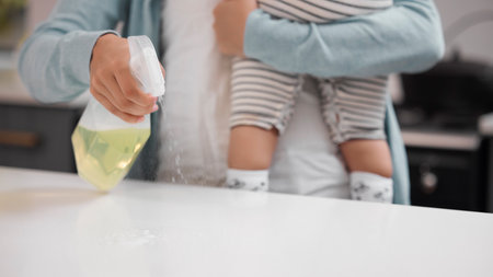 Keeping myself and my child safe. a mother cleaning her kitchen counter while holding her baby.