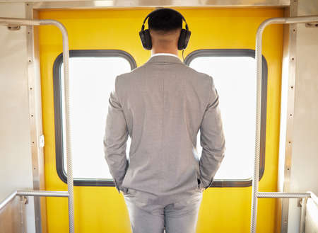 Another door of opportunity will open for him. Rearview shot of a young businessman wearing headphones while standing at the doorway of a train during his commute.の写真素材