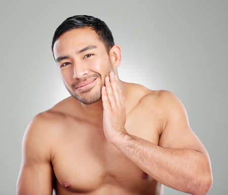 They call me Mr Smooth. Studio shot of a handsome young man touching his face against a grey background.の写真素材