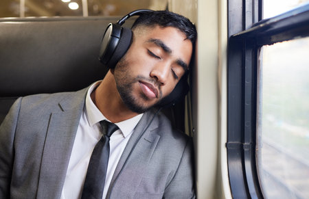 Catching up on some rest while he can. a young businessman wearing headphones while sleeping on a...