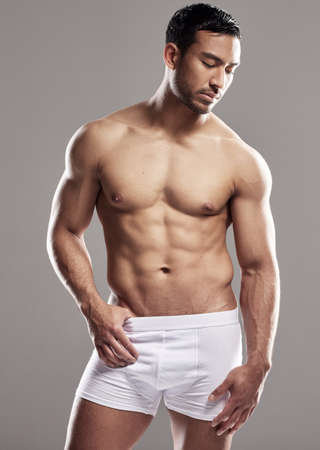 In awe of his magnificent physique. Studio shot of a muscular young man posing against a grey background.の写真素材