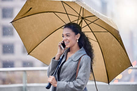 Im caught in the rain. a young woman holding an umbrella while on a call in the rain.