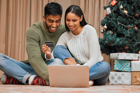 We can shop for everyone online. a young couple using a laptop and credit card during Christmas at home.の写真素材