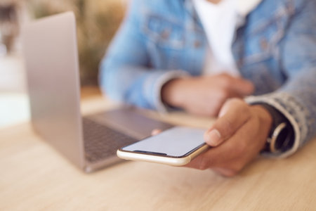 Texting my way to success. a man using his smartphone and laptop to work in a coffee shop.