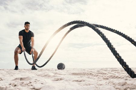 Im stronger than the voice telling me to quit. a sporty young man exercising outside with heavy ropes.の写真素材