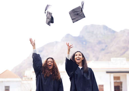 Graduation is better when we do it together. two young women throwing their caps in the air on...
