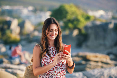 Beautiful woman using smartphone texting on beach at sunset