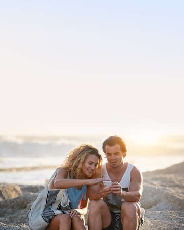 Young couple using smartphone on beach at sunsetの写真素材
