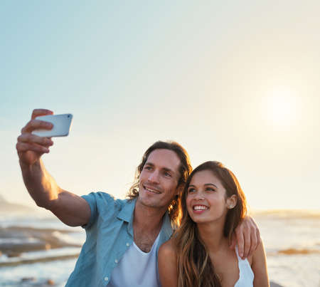 happy couple taking photo using smartphone on beach sharing romantic vacation togetherの写真素材