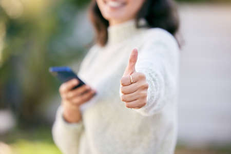 Spread likes online like its confetti. a woman using her cellphone and showing thumbs up while standing outside.の写真素材