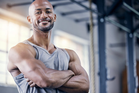 I can help you build a body like mine. Portrait of a muscular young man standing with his arms crossed in a gym.の写真素材