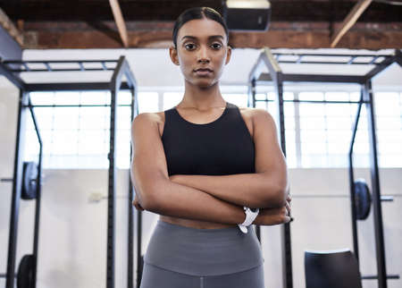 Serious about her fitness. Portrait of a sporty young woman standing with her arms crossed in a gym.の写真素材