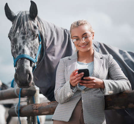Can you make it look like he loves me. an attractive woman using her cellphone while posing with a horse in an enclosed pasture on a farm.の写真素材