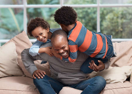 Wrestling time. a father playing with his two little sons on a sofa at home.の写真素材
