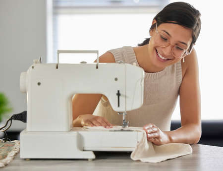 Adventure begins when I enter my sewing room. a young woman using a sewing machine in her workshop.の写真素材