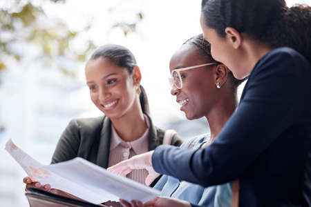 This plan looks great. a group of businesswomen going through paperwork against a city background.の写真素材