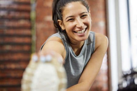 Warmup well before you start. Portrait of a sporty young woman stretching her legs while exercising in a gym.の写真素材