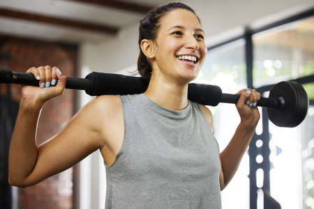 Strength training makes your joints stronger. a sporty young woman exercising with a barbell in a...