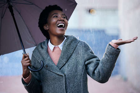 Who needs sun to have fun. a young businesswoman using an umbrella to cover with while going for a walk in the rain against an urban background.の写真素材