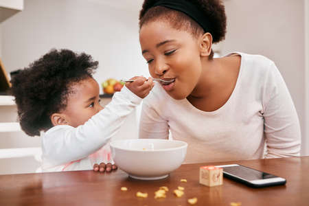 Here taste this mom. a little girl feeding her mom cereal.