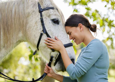 She enjoys spending time with her horse. an attractive young woman standing with her horse in a forest.の写真素材