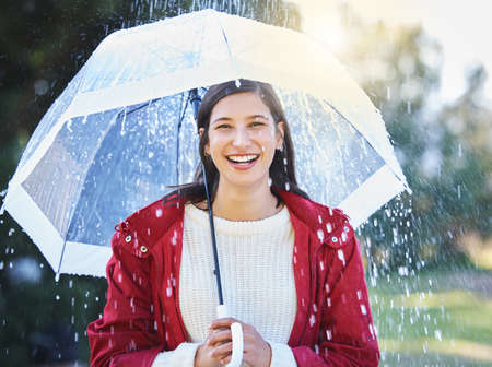 The rain cant get me now. a young woman holding an umbrella in the rain outside.