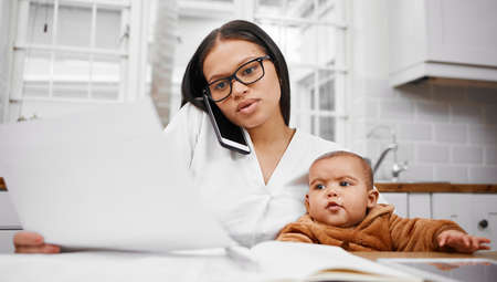 Being a mother should be a superpower. a young woman going through paperwork while holding her son...