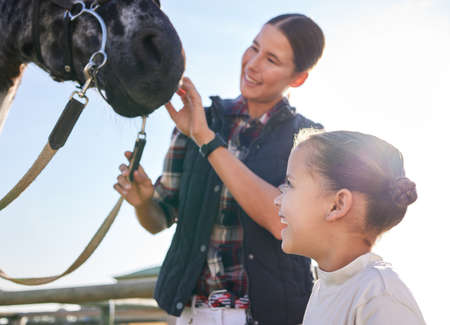 See Hes friendly. an attractive young woman and her daughter petting a horse outside on the ranch.の写真素材