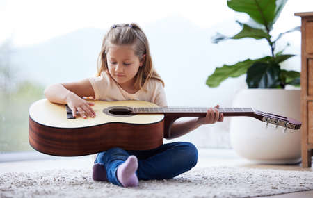 Shes found a new hobby. a little girl playing a guitar at home.の写真素材