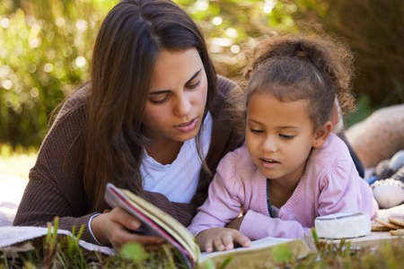 Story time in the park. Full length shot of an attractive young woman reading to her daughter while...